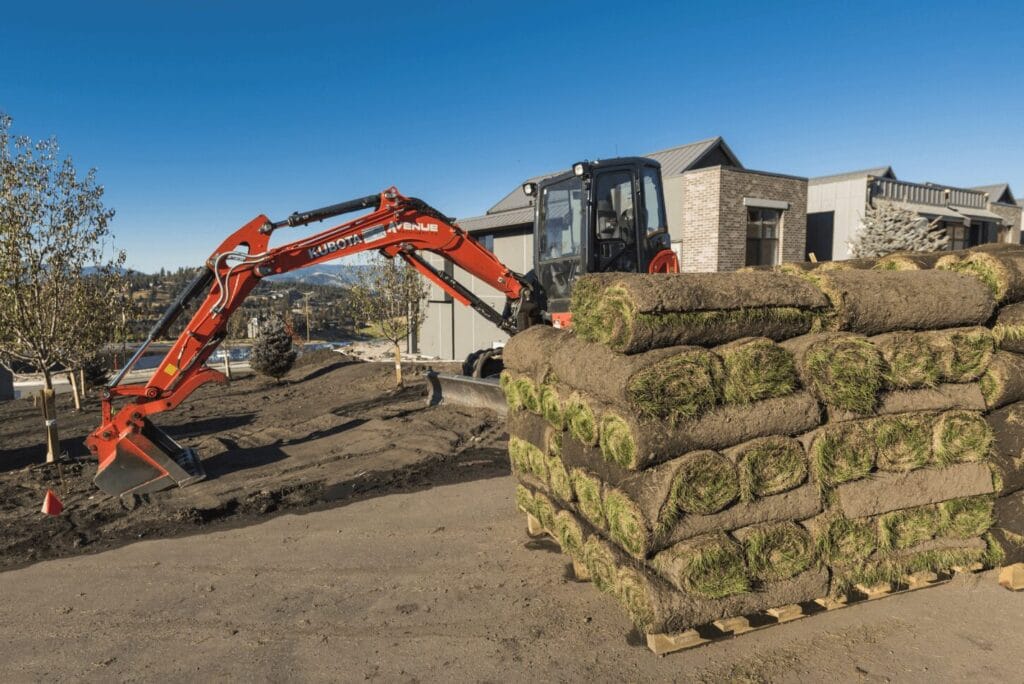 An excavator digging a foundation on a residential lot in Kamloops BC, with graded soil and a partially open excavation